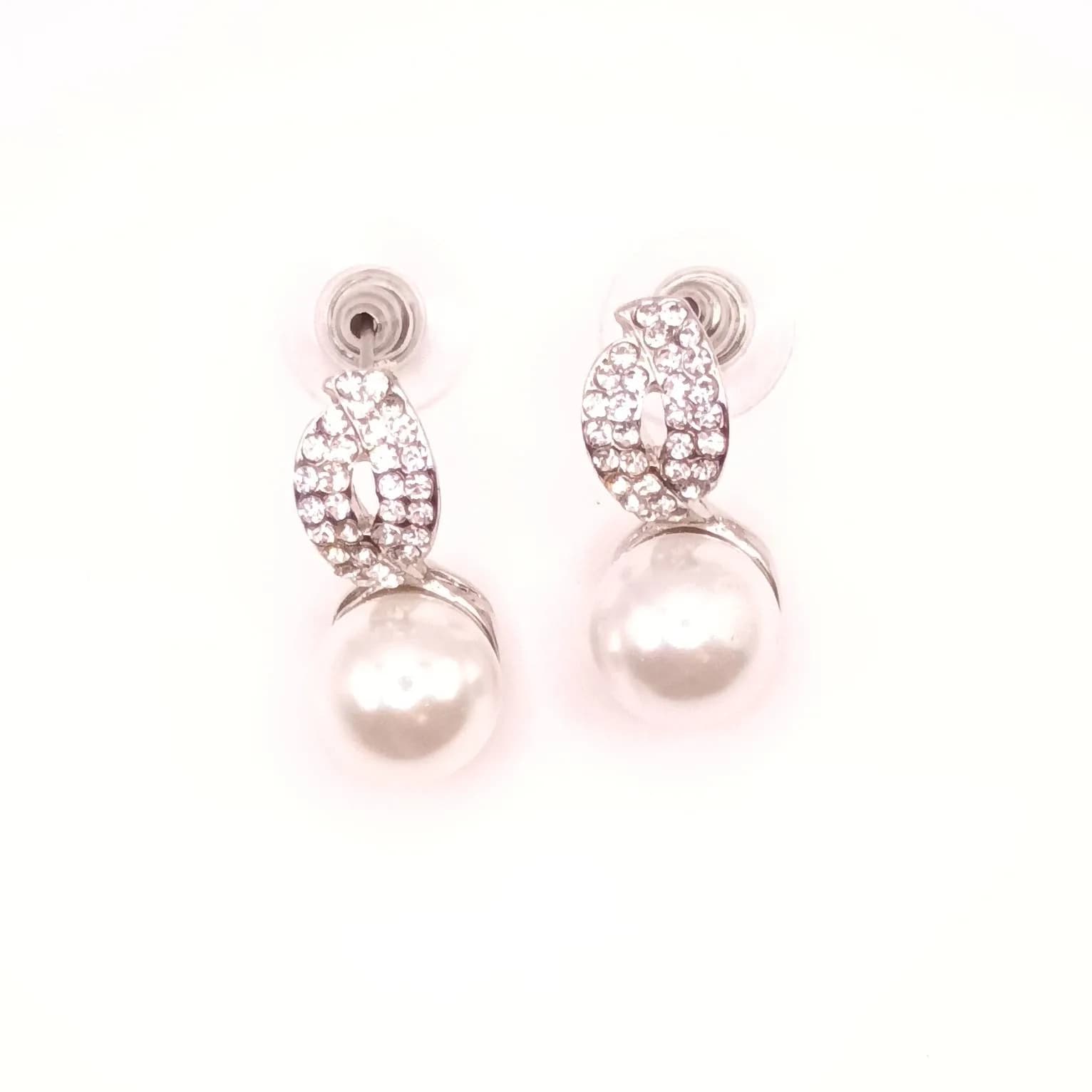 Paire de boucles d'oreilles à perle nacrée surmontée d'un motif torsadé pavé de pierres scintillantes, vue de face.