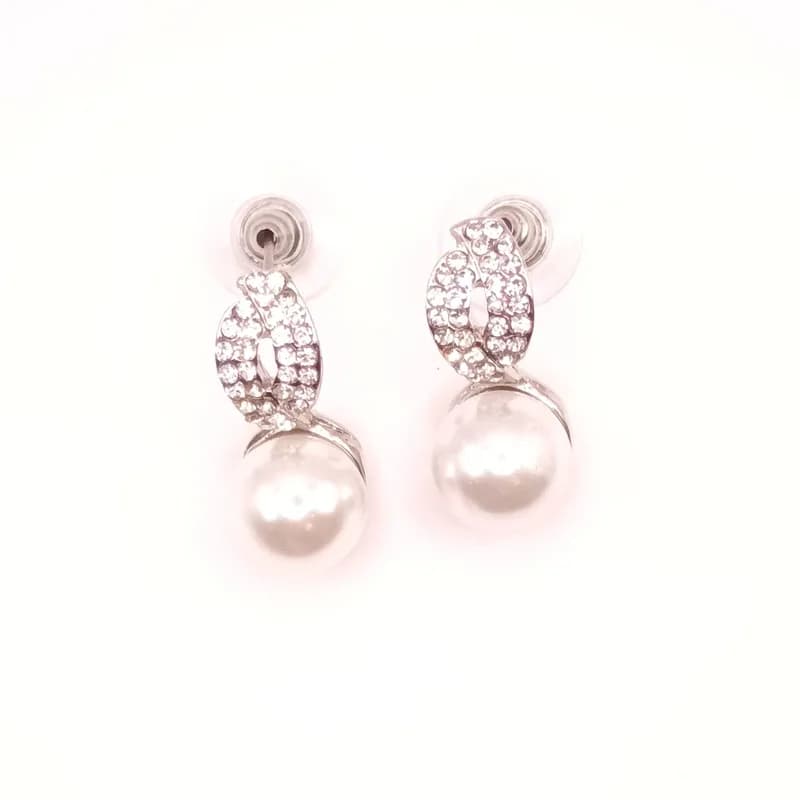 Paire de boucles d'oreilles à perle nacrée surmontée d'un motif torsadé pavé de pierres scintillantes, vue de face.