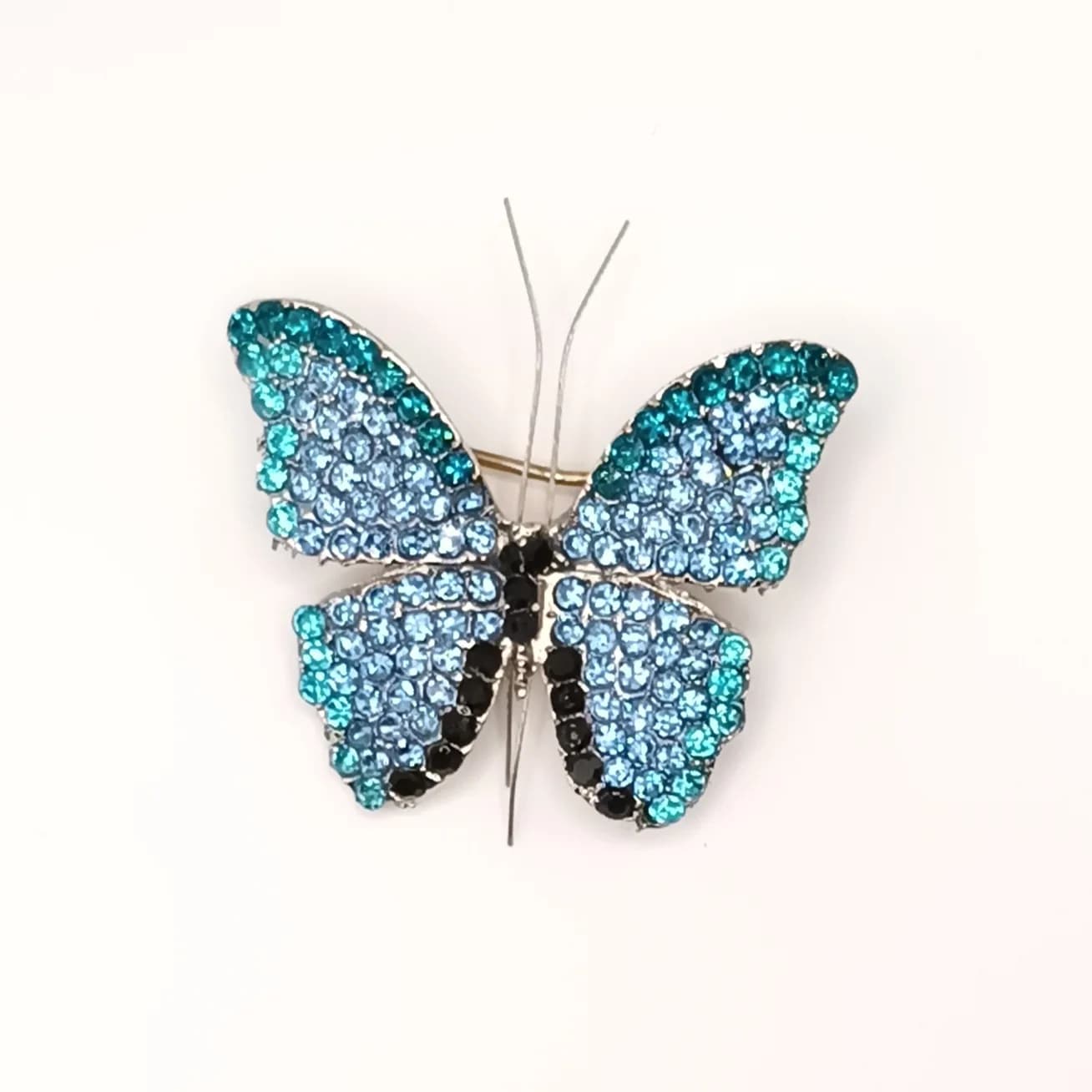 Broche papillon pavée de pierres scintillantes bleues et turquoise vue de face.