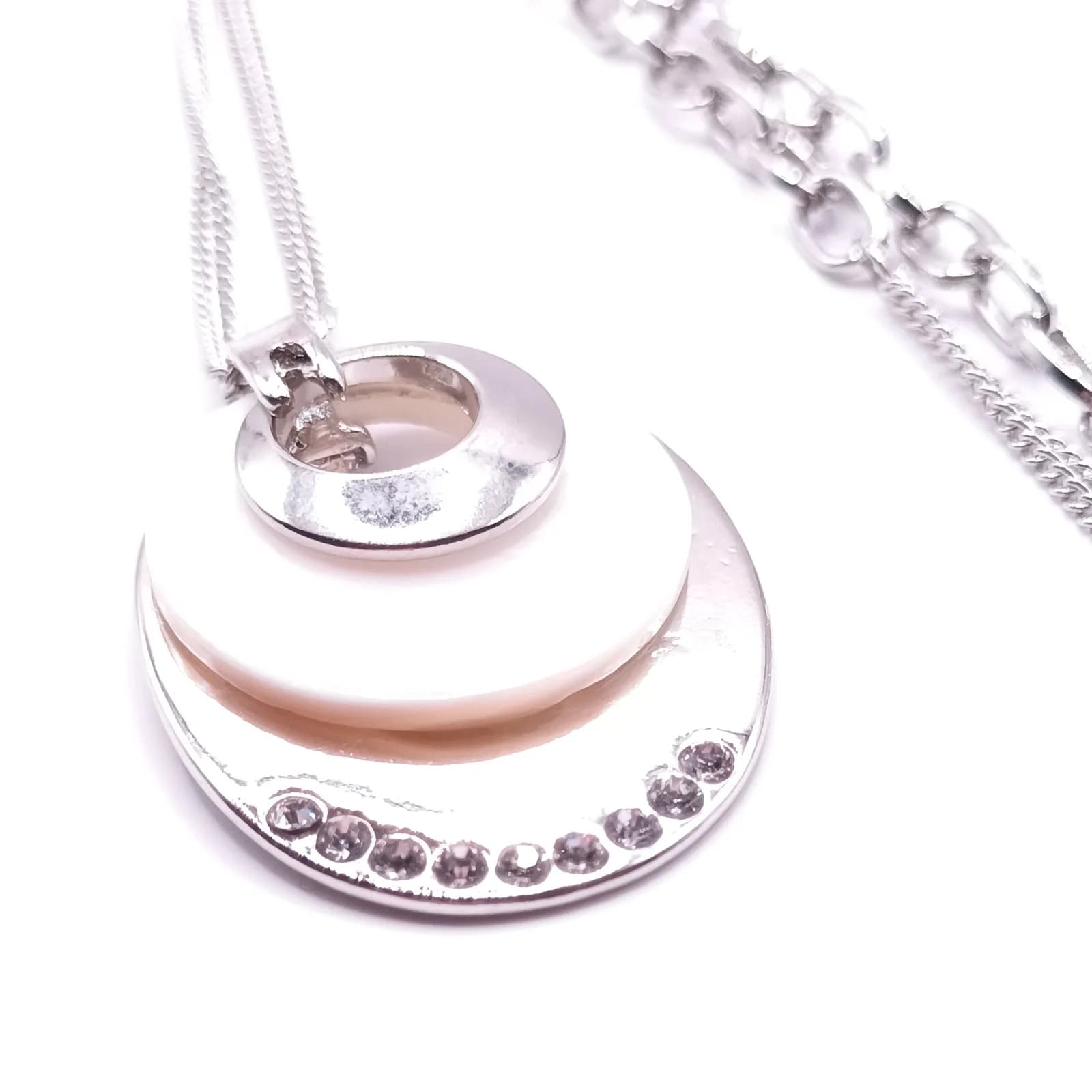 Gros plan sur les pierres scintillantes et le disque nacré du pendentif ovale.
