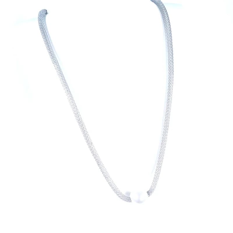 Collier à maille argentée et perle blanche porté sur un buste blanc.