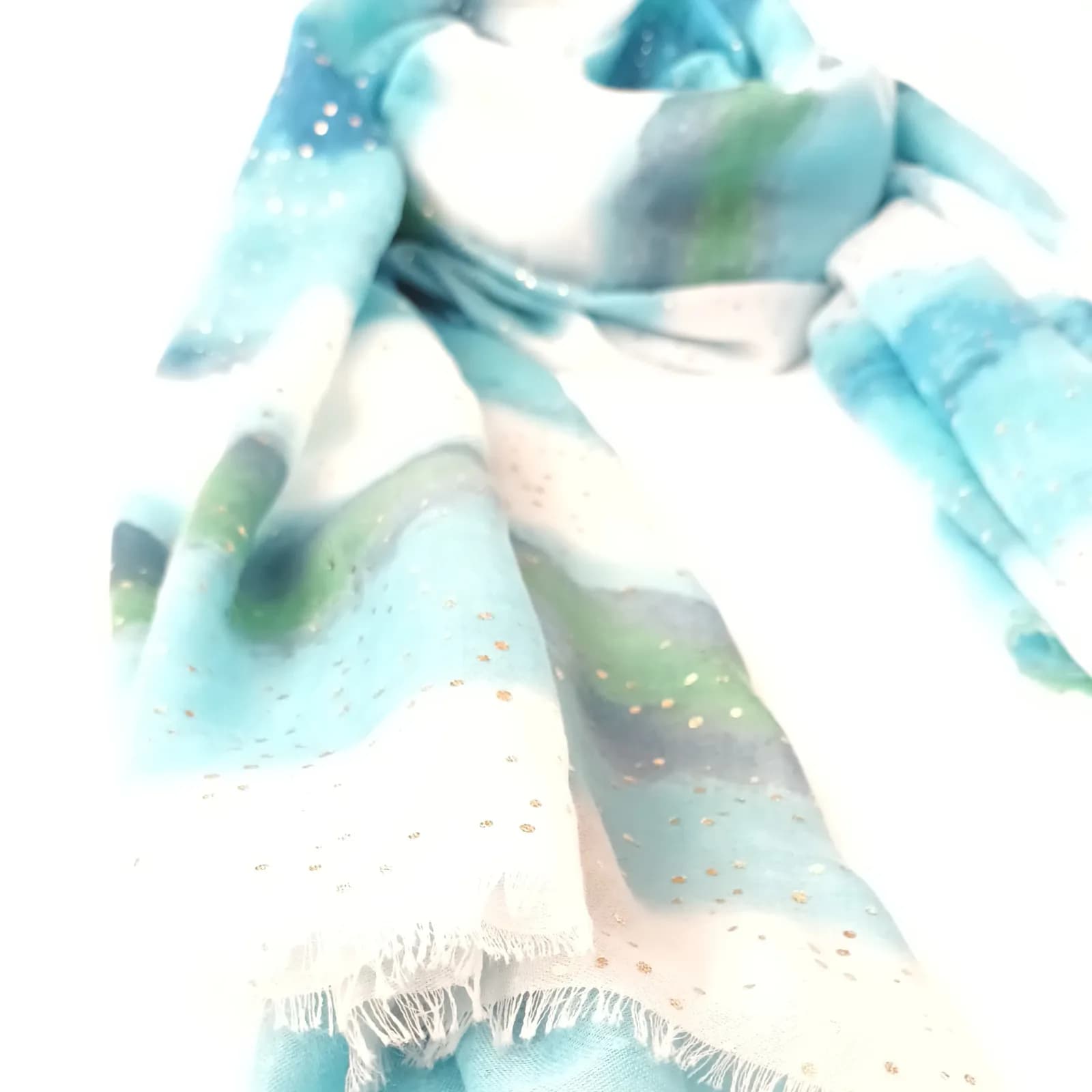 Détail des bords frangés et des pois scintillants du foulard turquoise.
