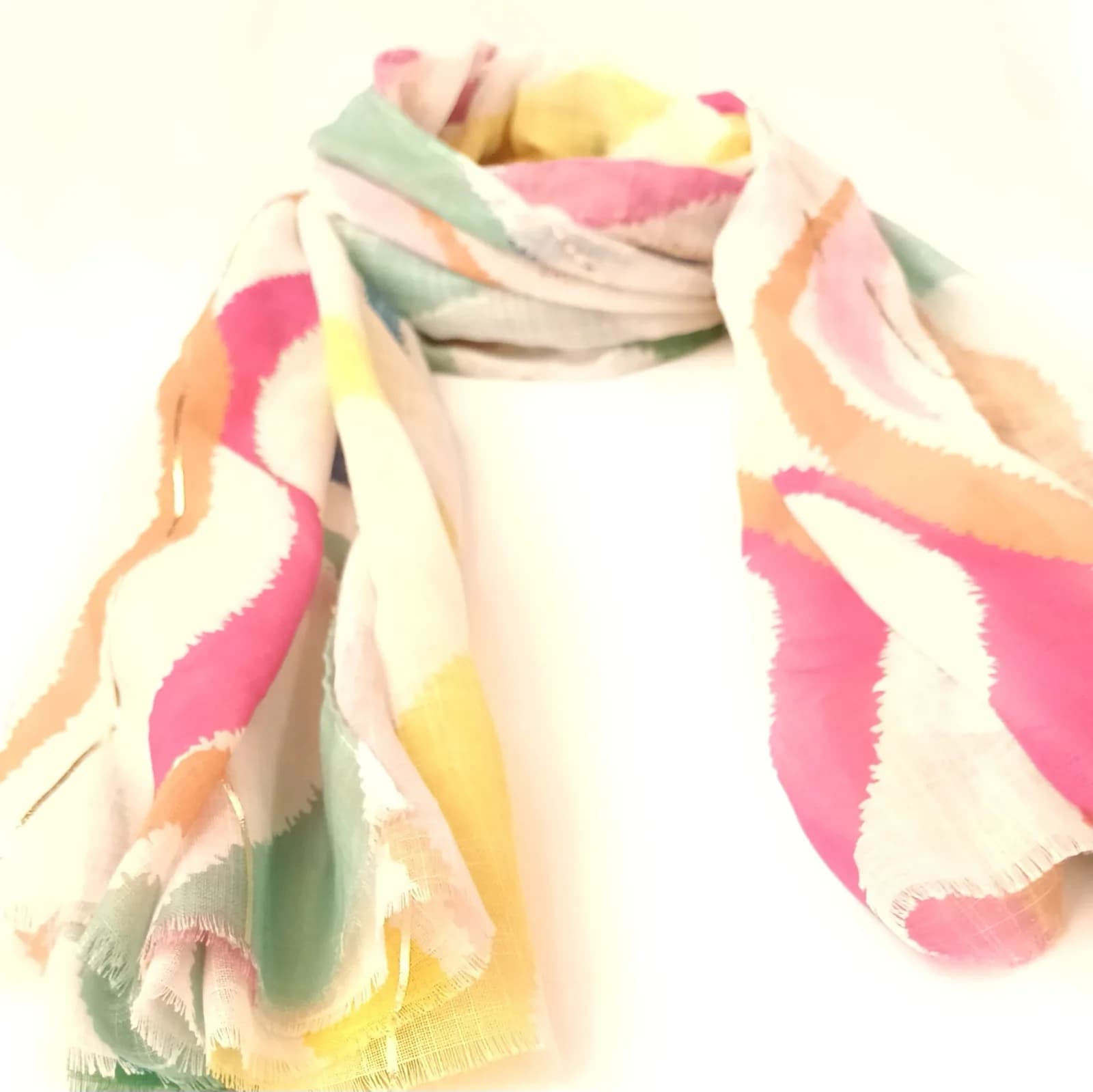 Foulard à vagues roses, jaunes et pêche, drapé et vu de biais, avec ses bords frangés.
