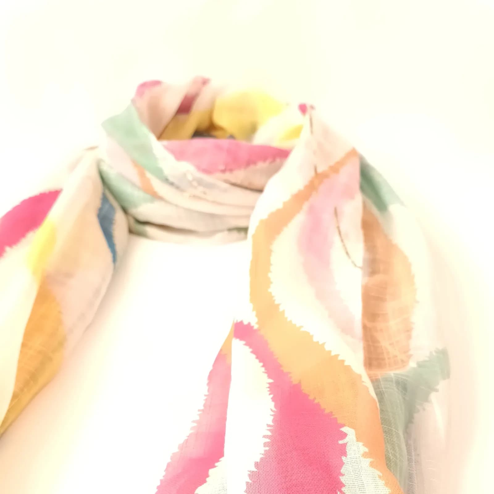 Vue rapprochée du nœud du foulard ikat aux motifs rose, pêche et vert d'eau.