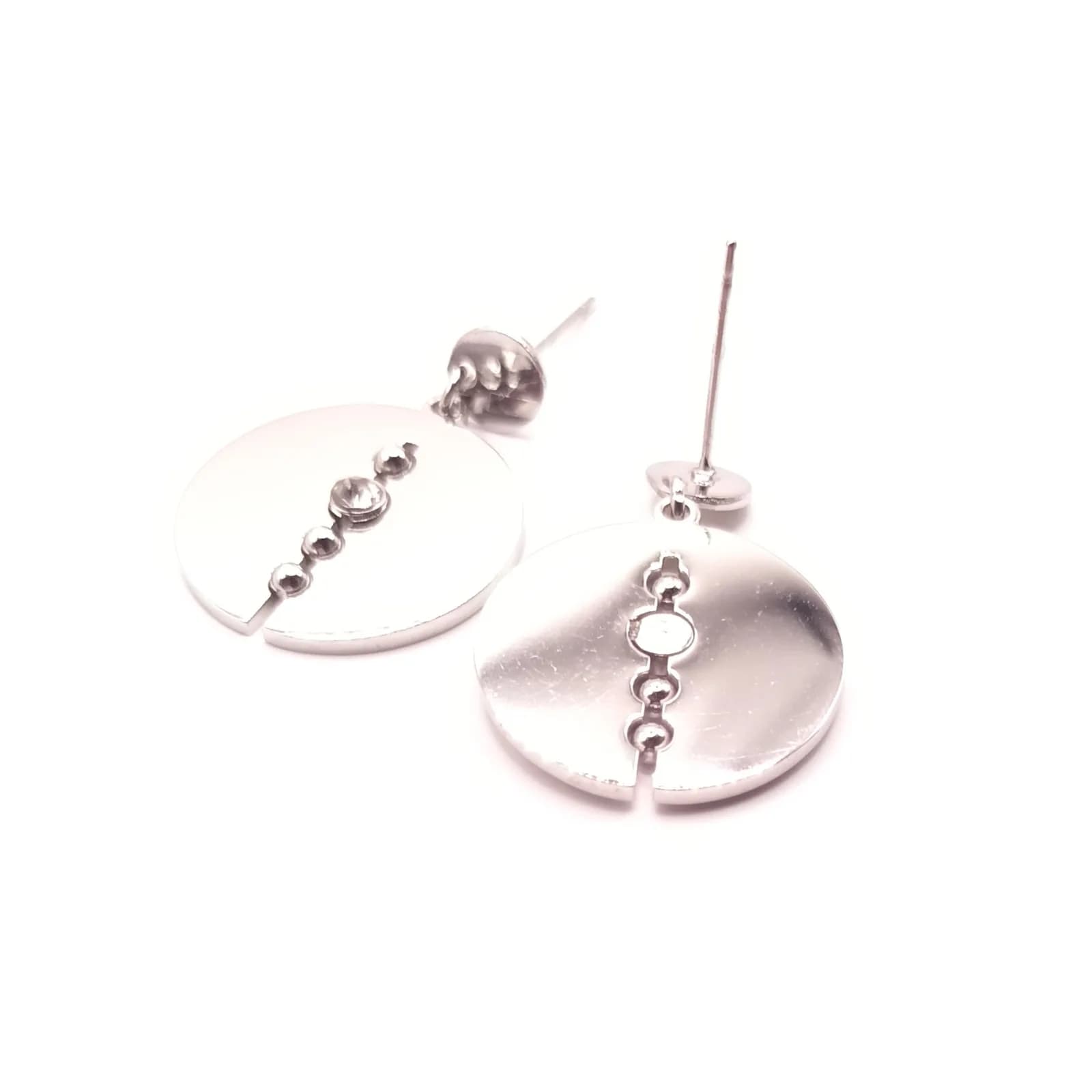 Boucles d'oreilles disque argenté posées à plat, ligne de perles et pierre scintillante au centre.