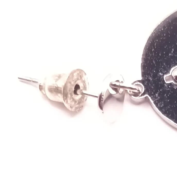 Gros plan sur la tige et le fermoir poussette d'une boucle d'oreille disque argenté.