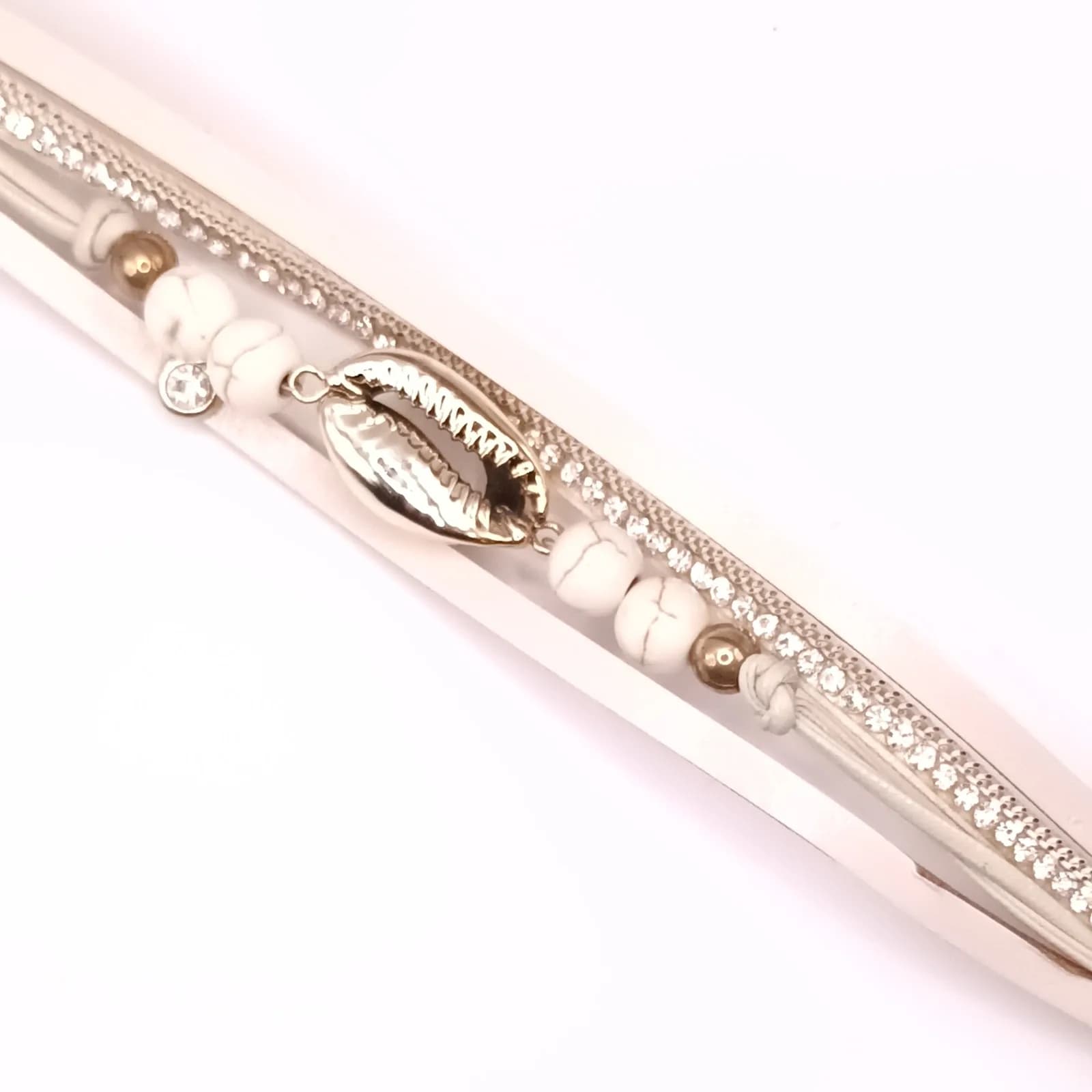 Détail du coquillage cauri doré et des perles veinées blanches du bracelet