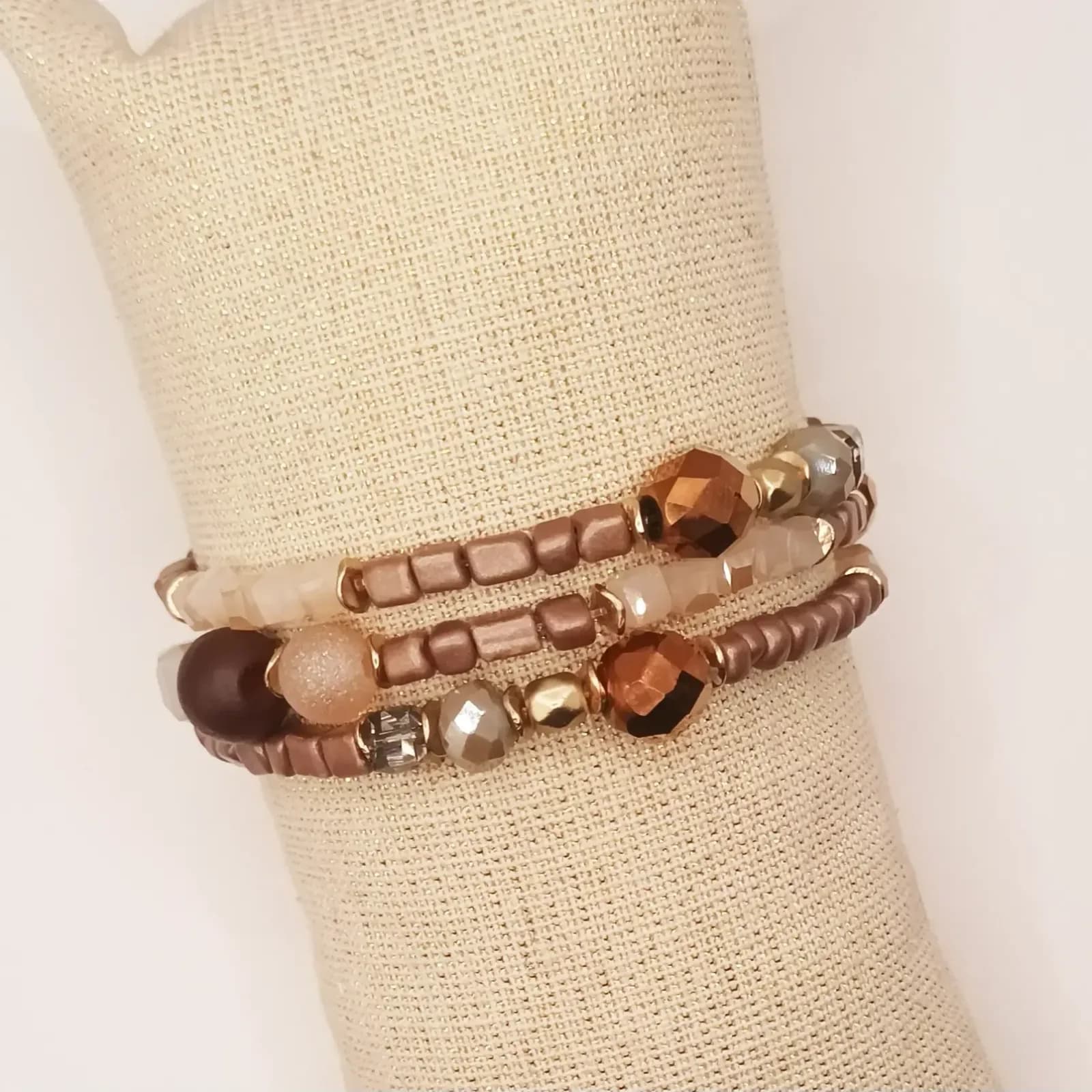 Trio de bracelets en perles marron, beige et cuivrées - porté sur un présentoir en lin, vue de face