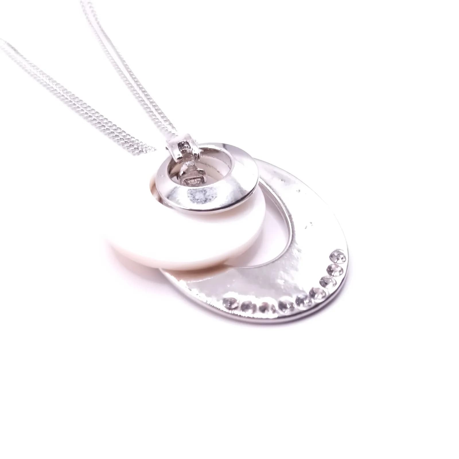 Pendentif ovale ton argenté avec disque nacré et rangée de pierres scintillantes vu de face.