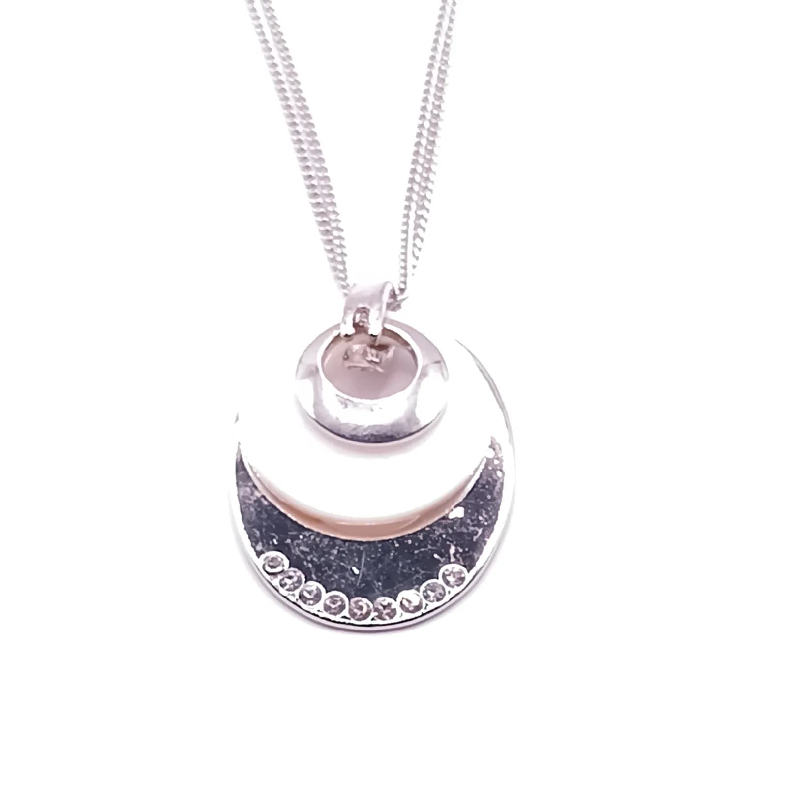 Collier à double chaîne fine et pendentif nacré posé sur fond blanc.