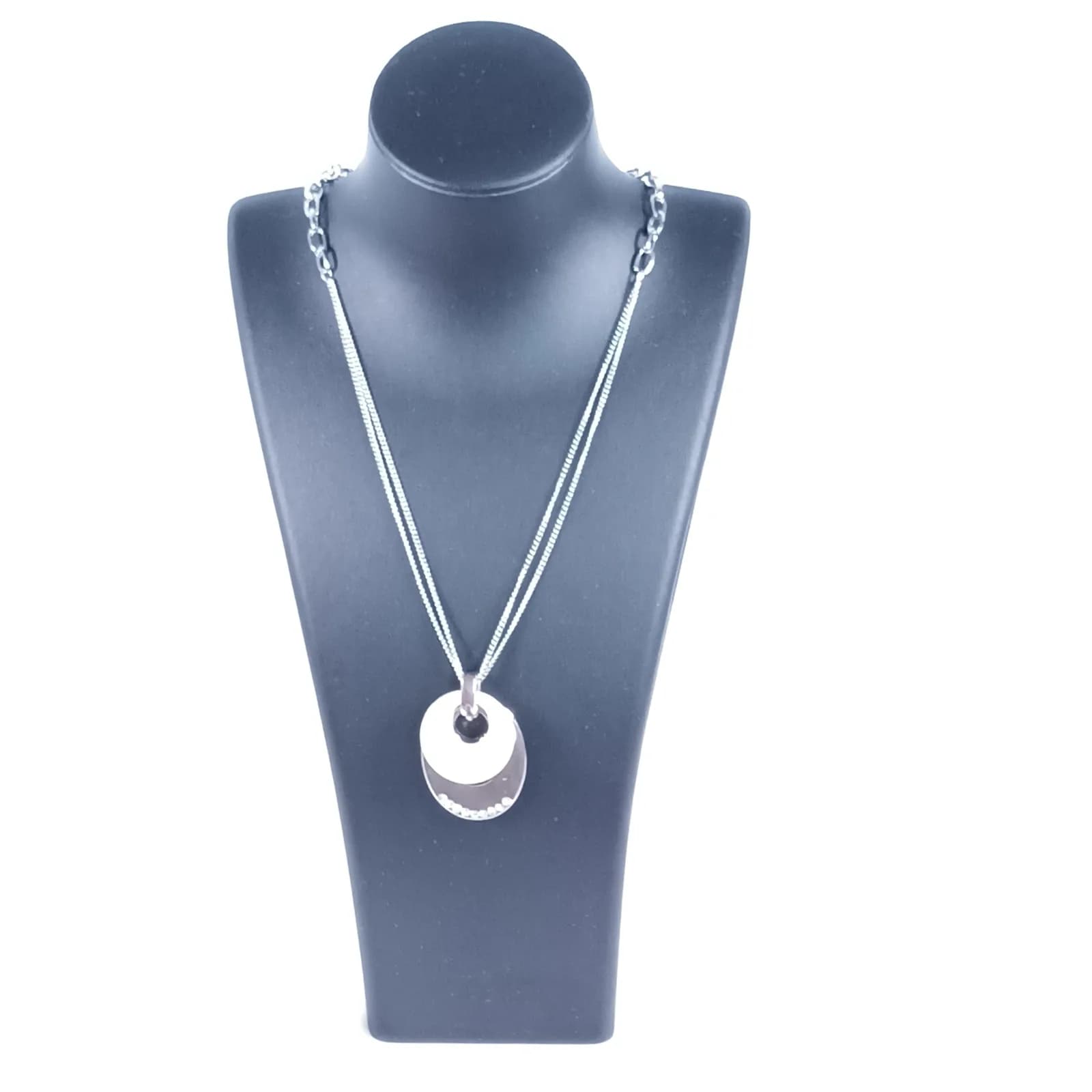 Collier à pendentif ovale ton argenté et disque nacré porté sur un buste noir.