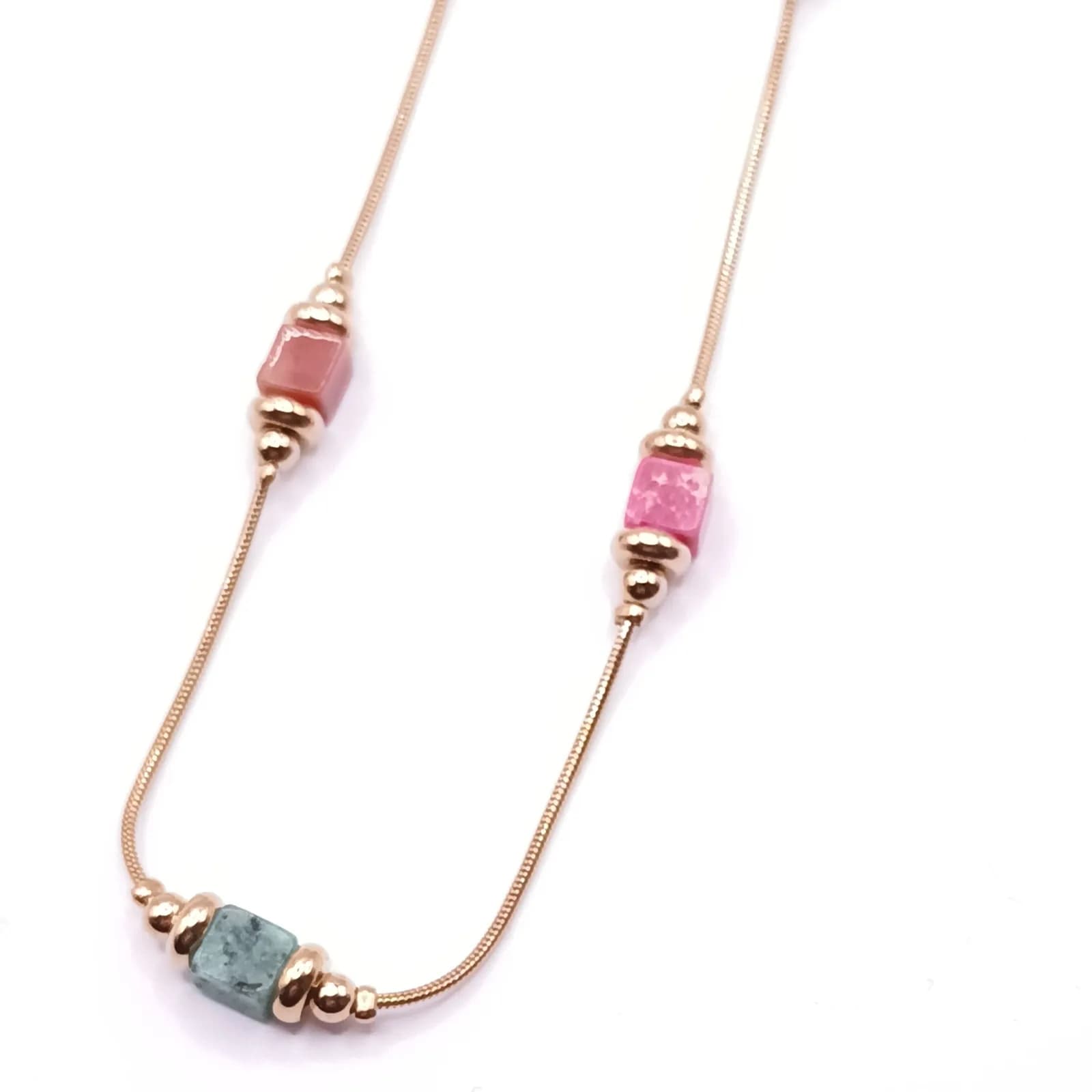 Gros plan sur les cubes corail, rose et vert entourés de perles ton or rose.