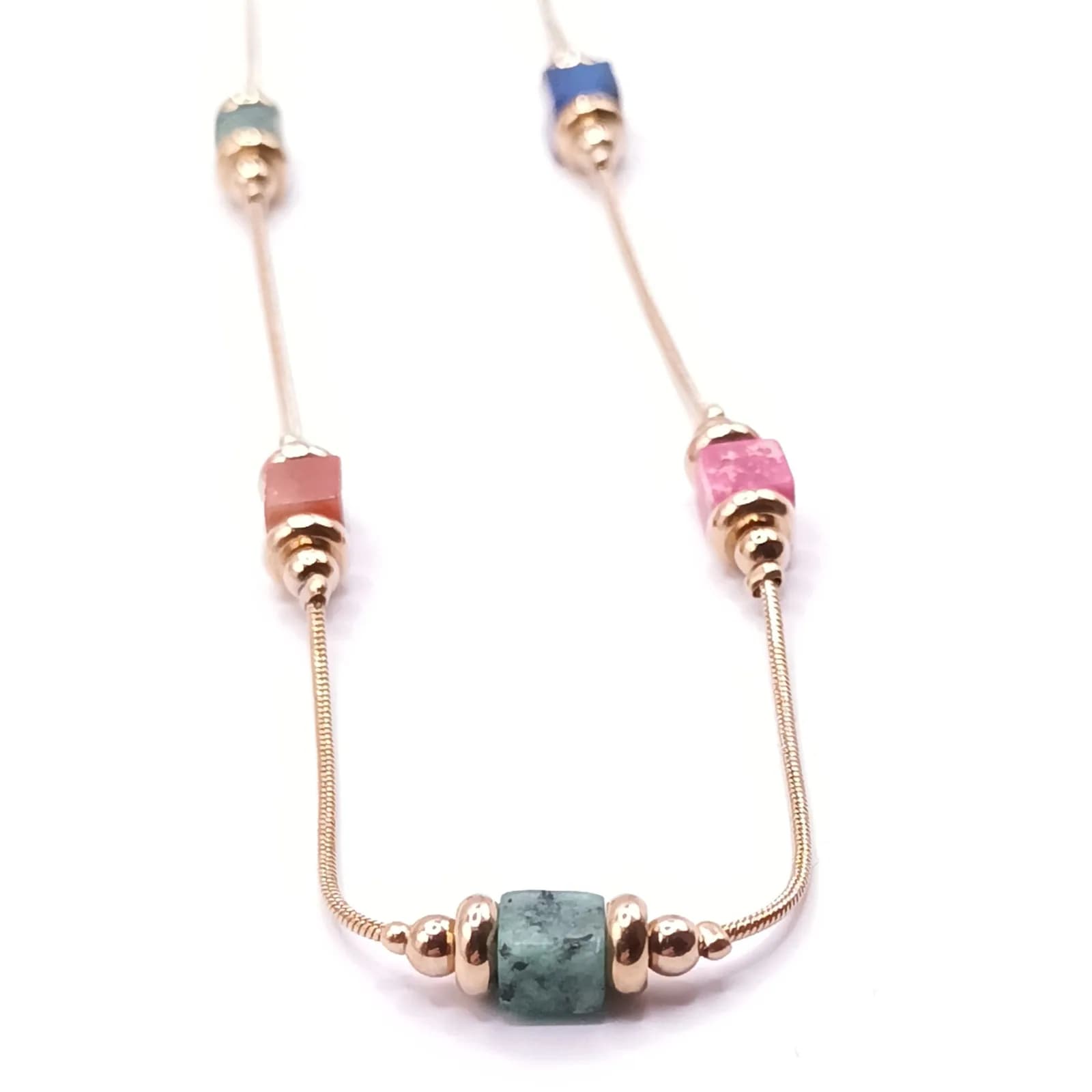 Collier à cubes colorés et perles brillantes posé sur fond blanc, vu en perspective.