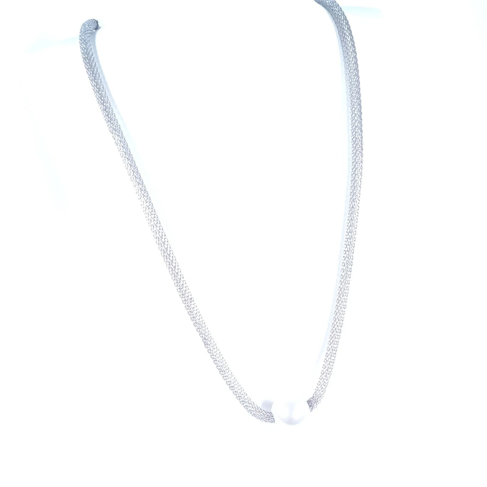 Collier à maille argentée et perle blanche porté sur un buste blanc.