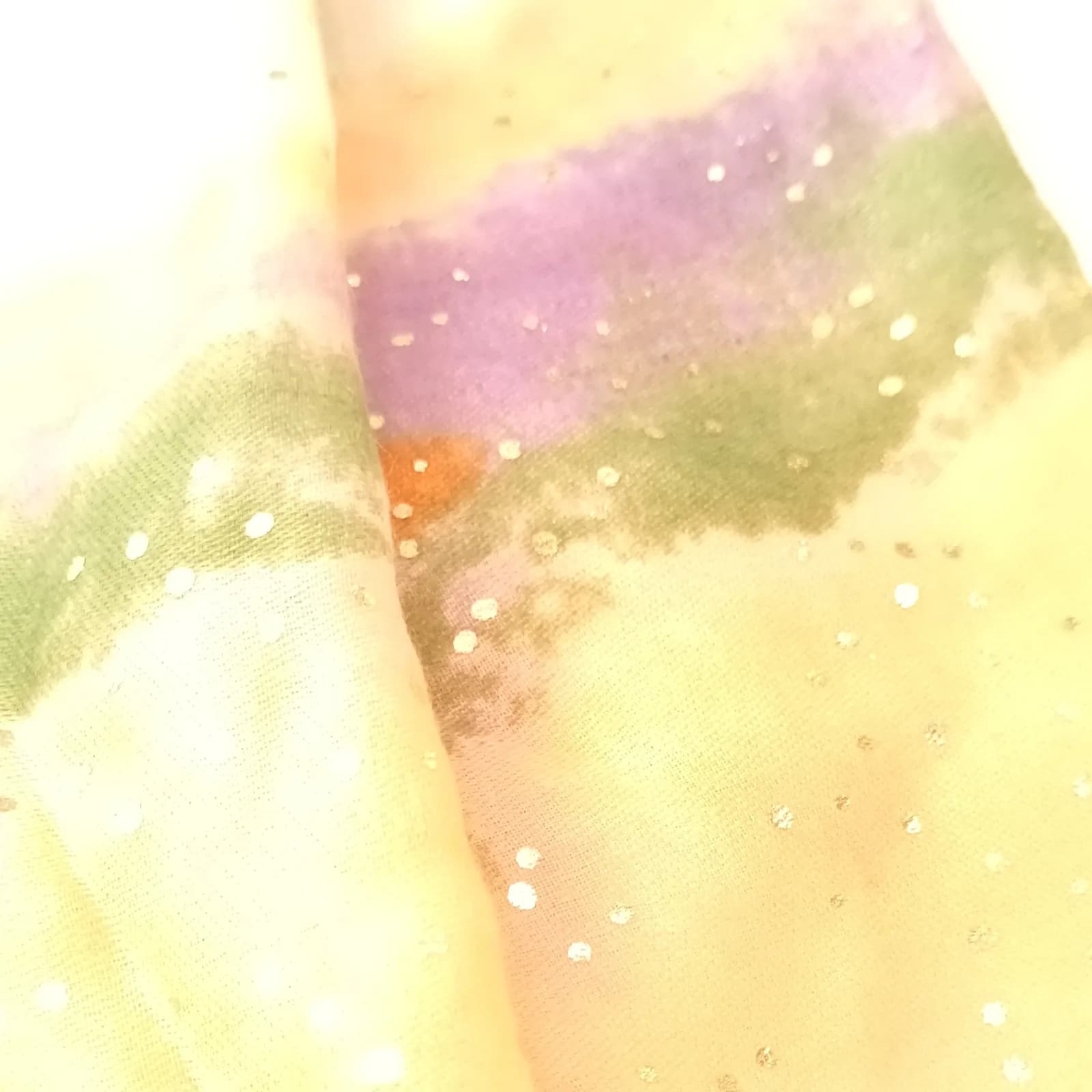 Gros plan sur les pois scintillants et les nuances lilas, vert et jaune du tissu.