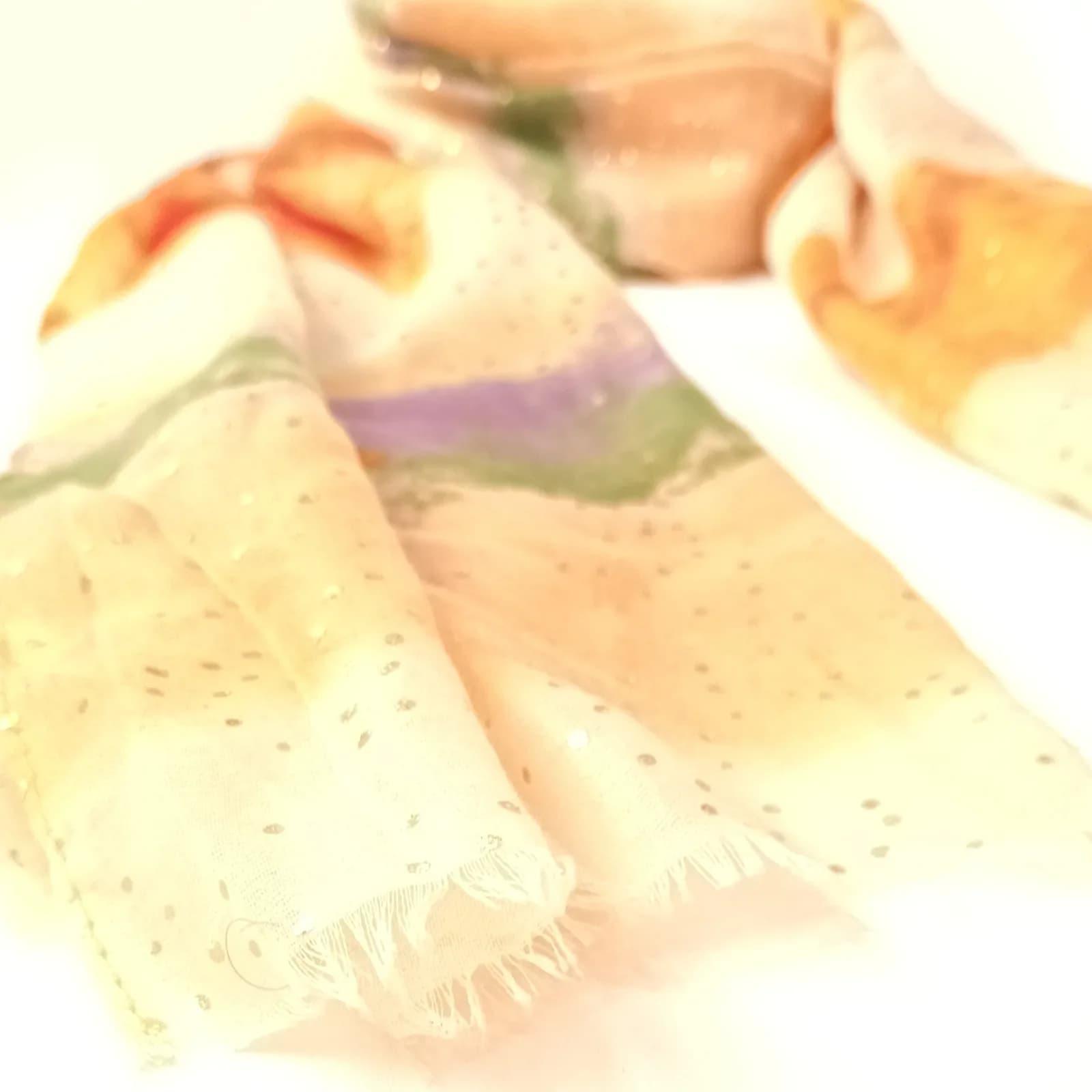Détail des bords frangés et des bandes vert et lilas du foulard ivoire.