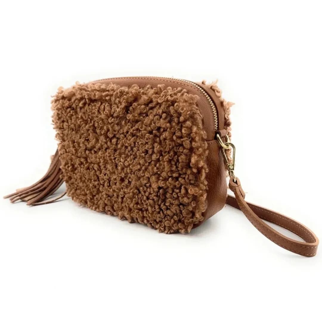 Sac rectangulaire à texture bouclette camel avec pompon, fermeture zippée dorée et dragonne assortie, vu de trois quarts sur fond blanc.