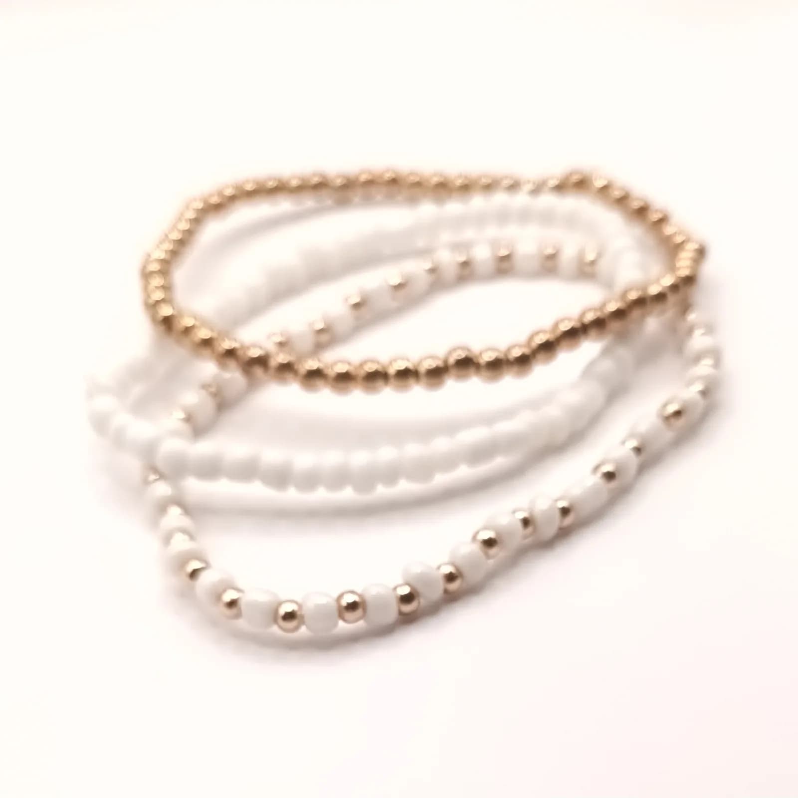 Trio de bracelets en perles blanches et dorées sur fil élastique